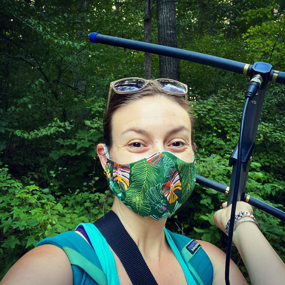 An image of Lydia working in the field carrying her equipment with the rainforest in the background.