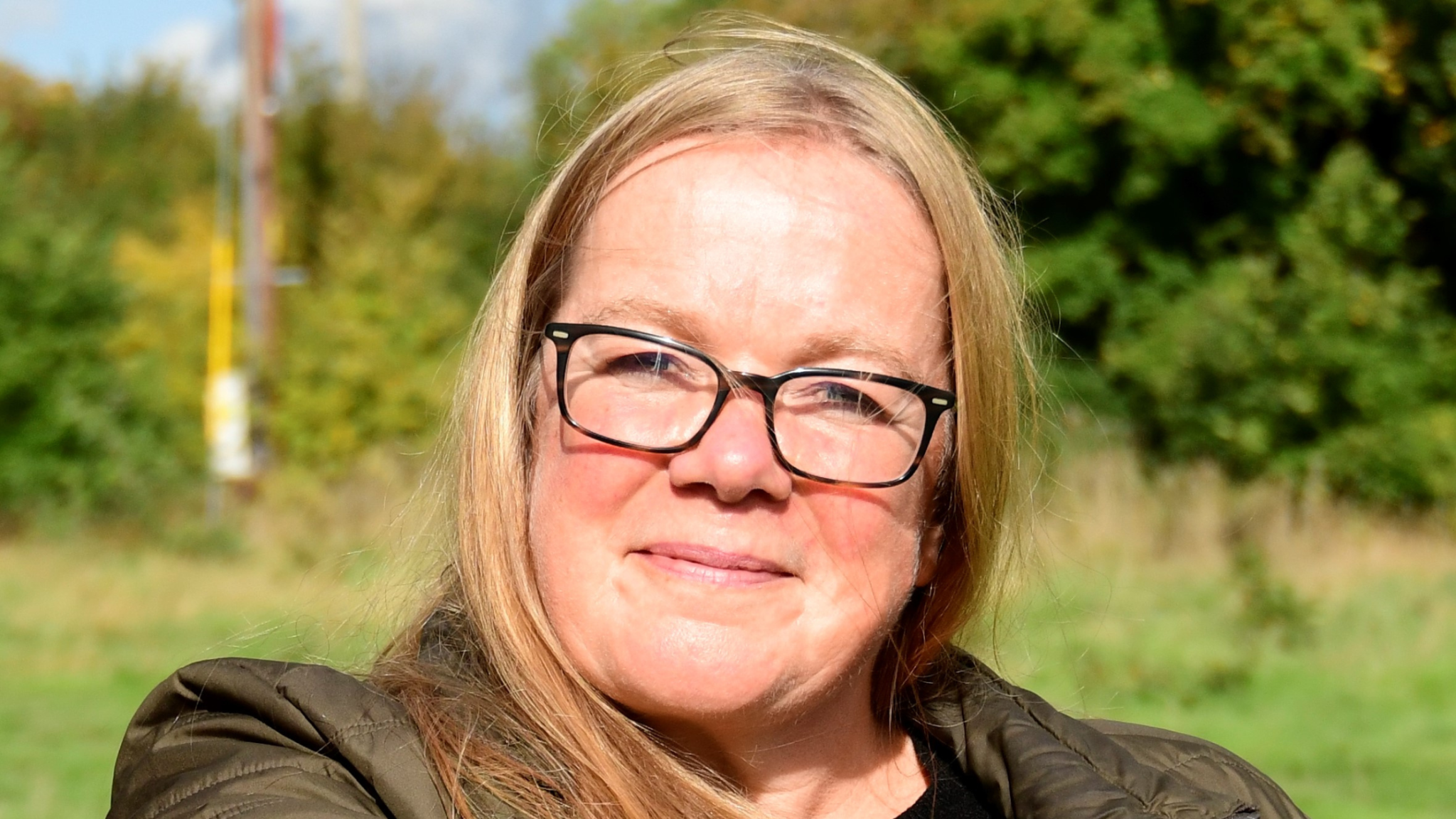 A portrait photo of Emma Marsh smiling at the camera outside with green trees behind her.