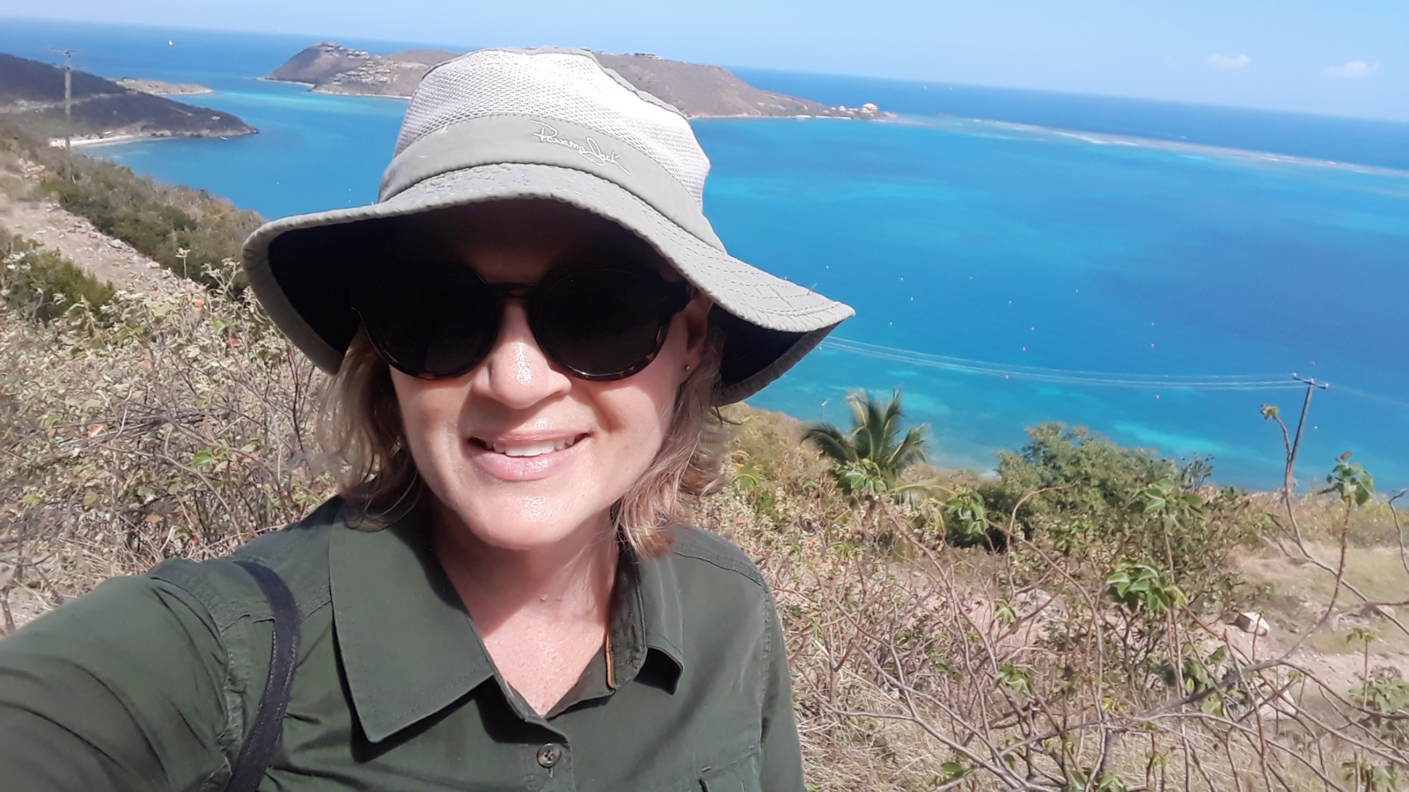 Nancy Pascoe at a coastal scrub habitat on a sunny day, with blue sea and an island in the distance.