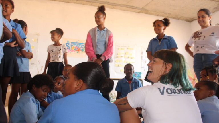 The picture is taken from behind. Yolanda, and environmental educator, is sitting around a group of teenagers, smiling, and paying attention to something that is going on next to them. The picture doesn’t show what are they laughing at.