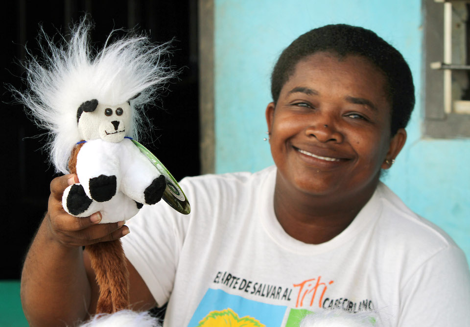 A local artisan holding up a handmade stuffed toy tamarin and smiling.