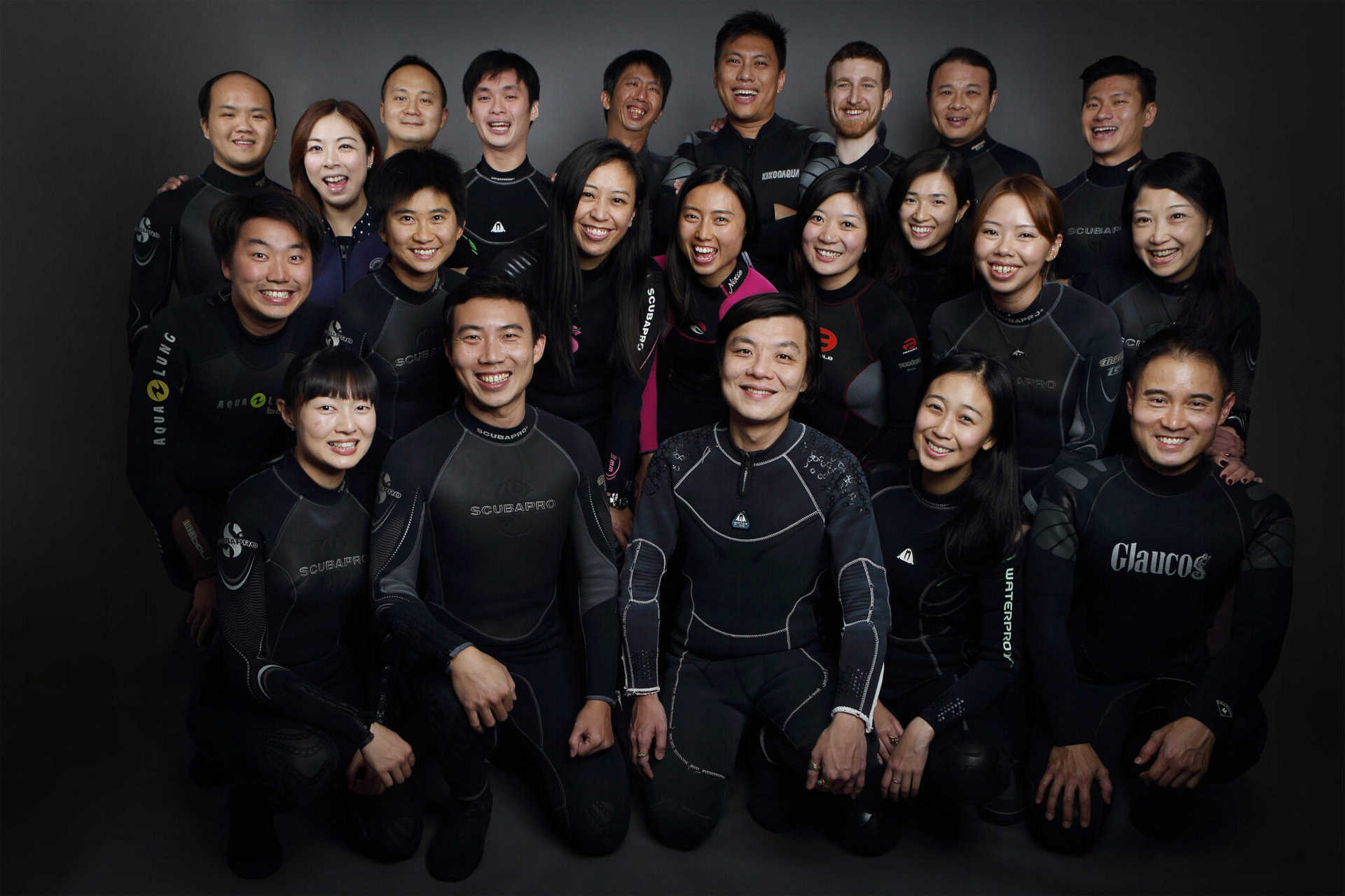 Stan is kneeling down; he is with a group of 22 colleagues and volunteers all involved with the 114°E Hong Kong Reef Fish Survey. They all are wearing their dive gear and looking at the camera. 