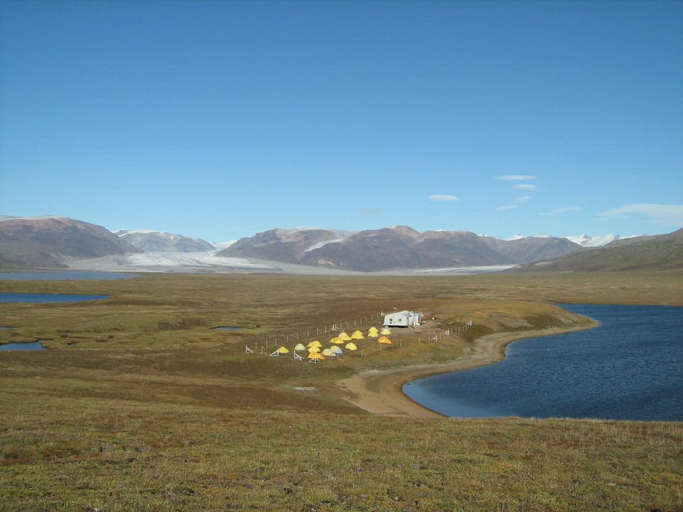 Landscape view of The Bylot Island Research Station in Canada, featuring small yellow tents and the research station building in a valley.