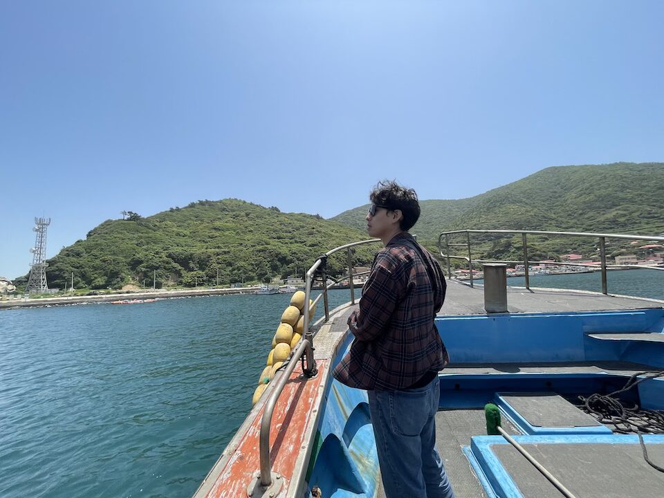 Conservationist Yongki Lee standing looking out at the water. In the background is a hill slide rising from the water. He is on a boat conducting fieldwork.