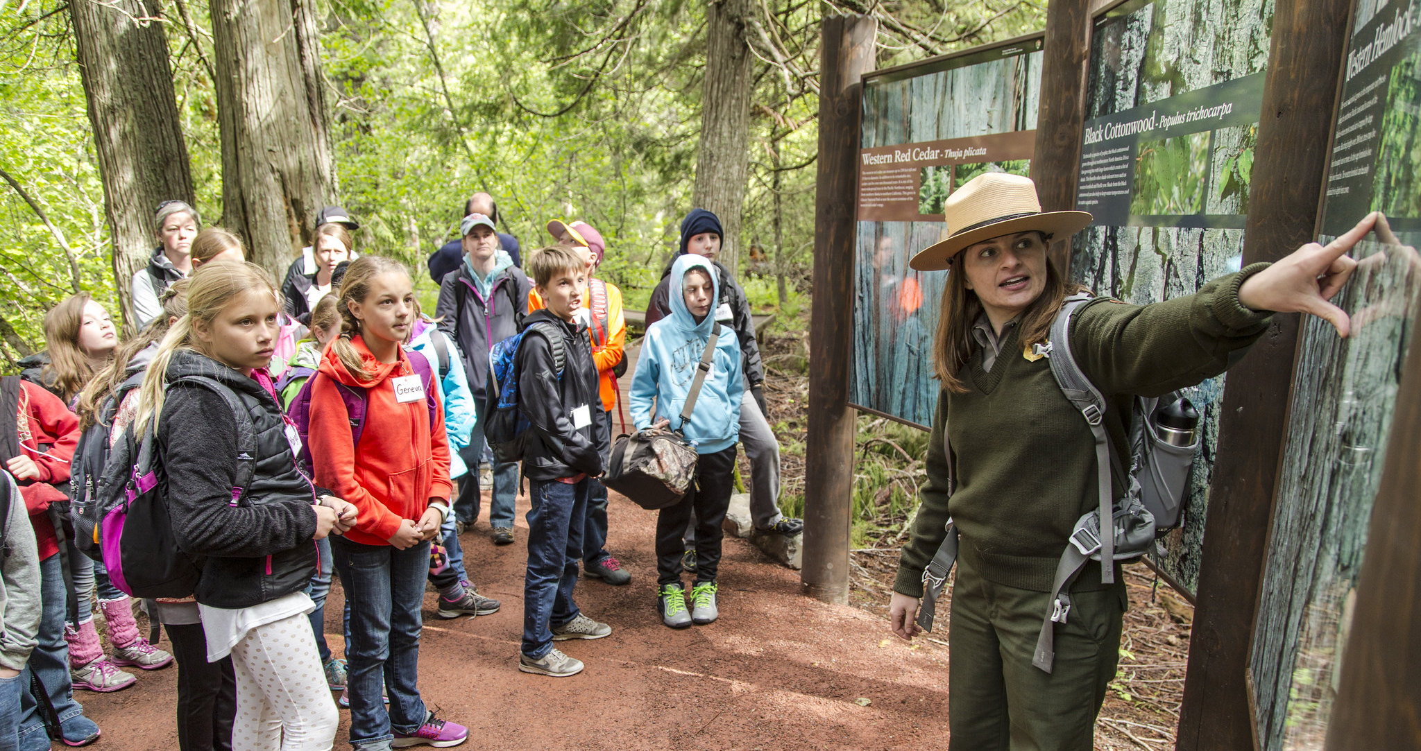 A park ranger pointing to a park sign and speaking to a group of young people. If you become a park ranger, you could help the public care about parks and nature.