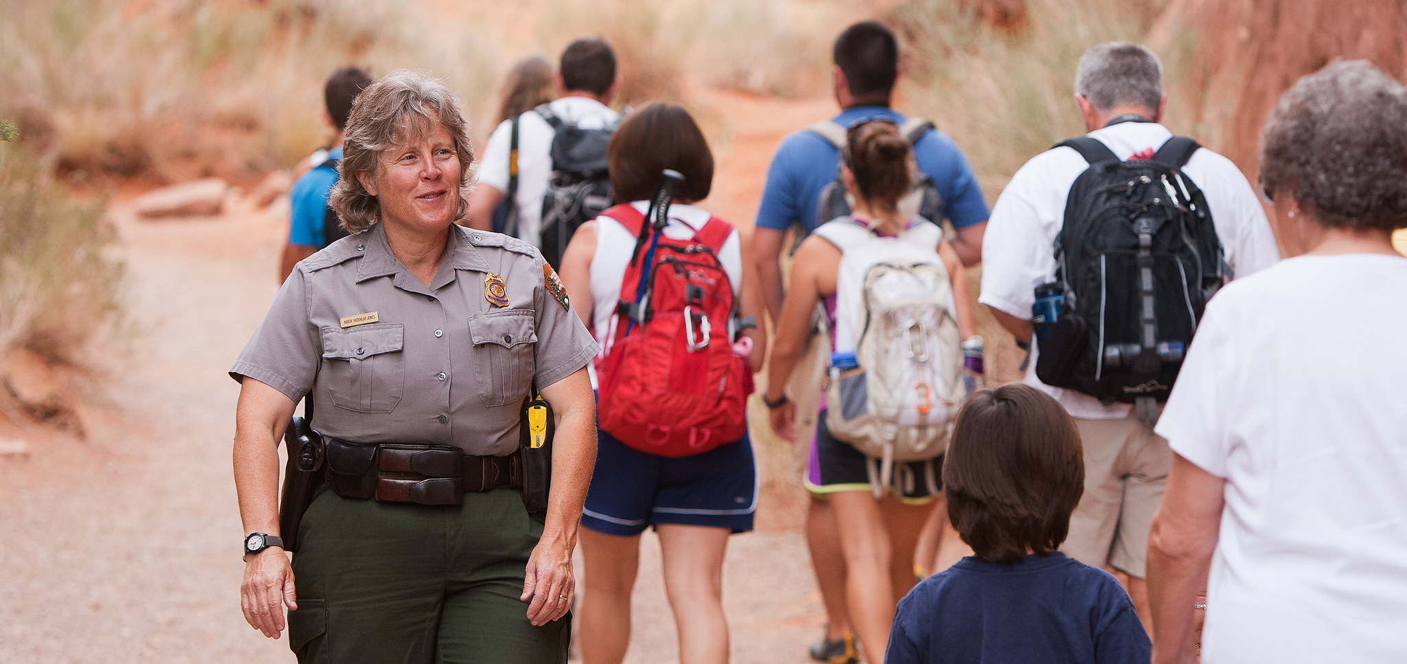 A woman forest ranger in uniform walking towards the camera amidst a group of park visitors.