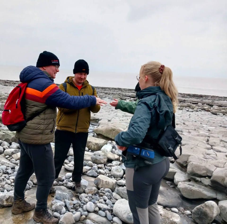 A woman stands with two volunteers on a shoreline.