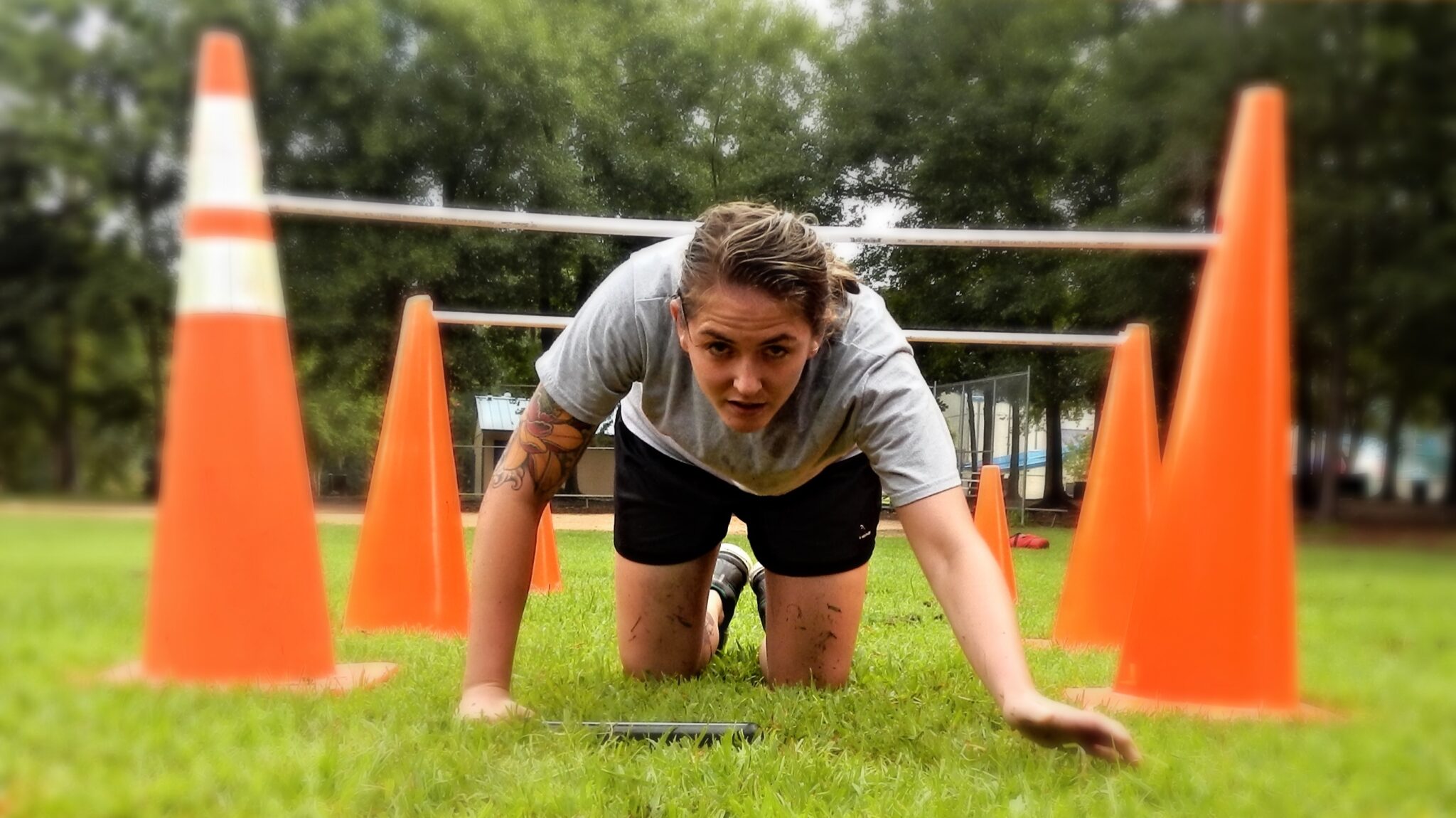 A woman crawling on hands and knees on grass in and obstacle course, training to become a conservation officer.