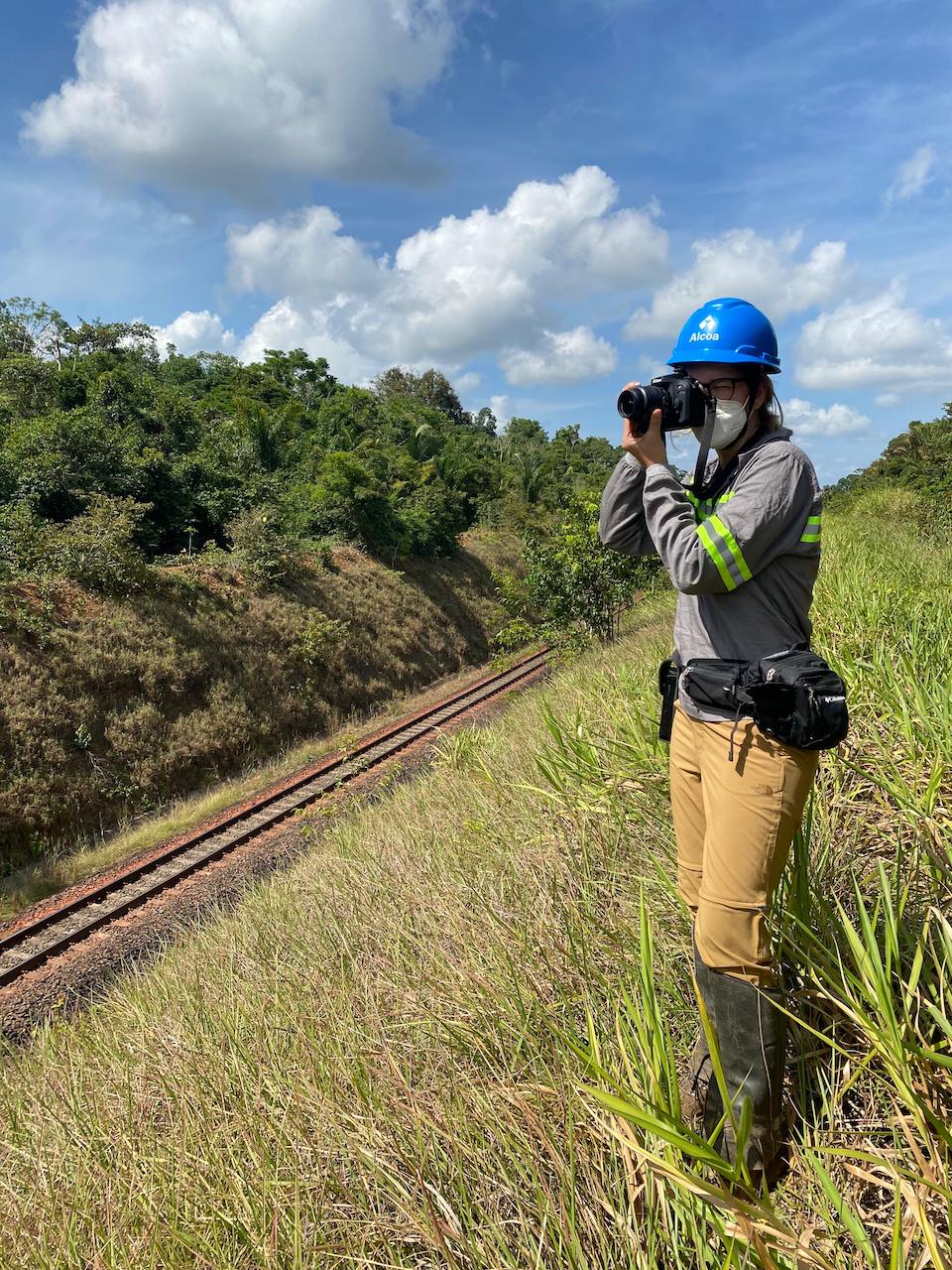 A female professional in hardhat and uniform conducting monitoring of a railway. She is holding a camera to her face.