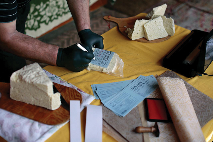 Person wearing black gloves labelling packaged cheese on a table with cheese blocks.