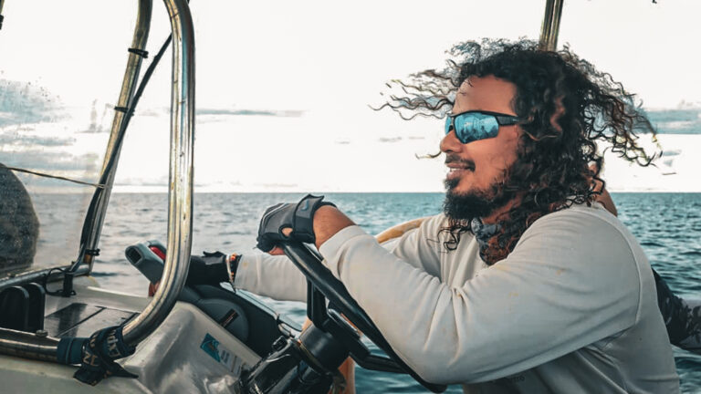 A man leans on the wheel of a boat, looking out over the ocean.