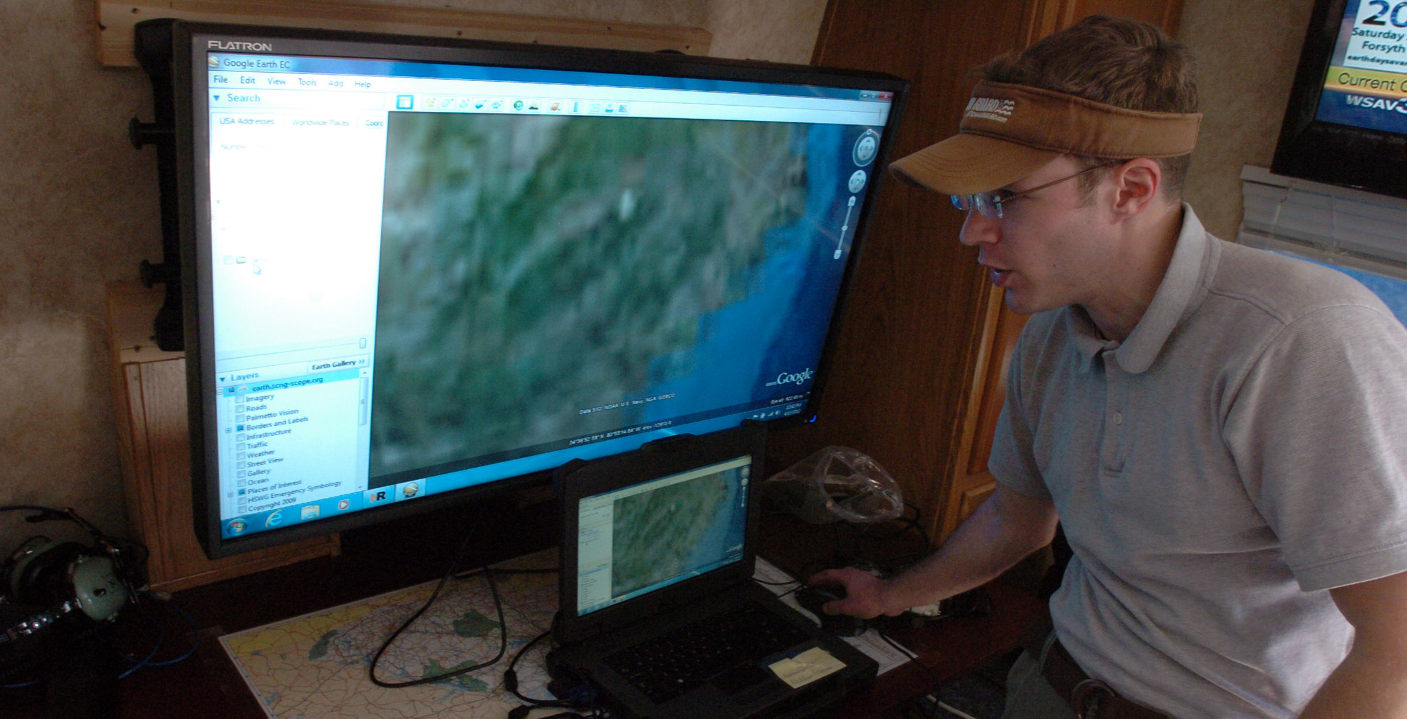A GIS Analyst standing in front of a large computer monitor showing a map.