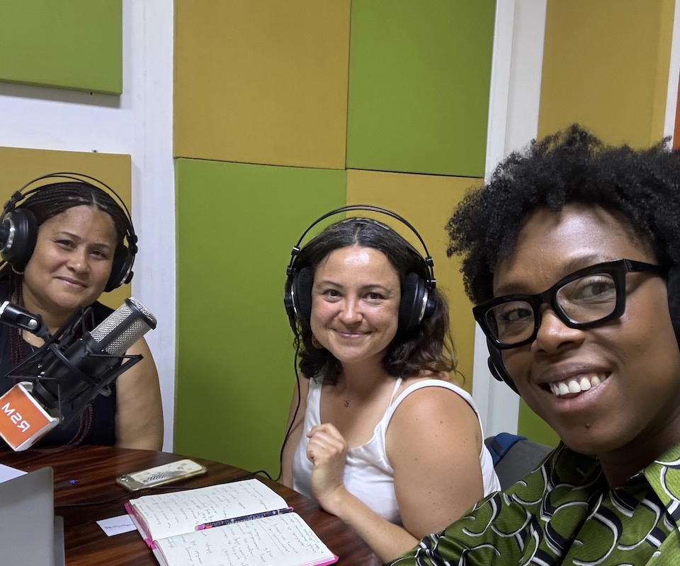 A female conservation geneticist and primatologist in a radio studio with a female director and a female singer.