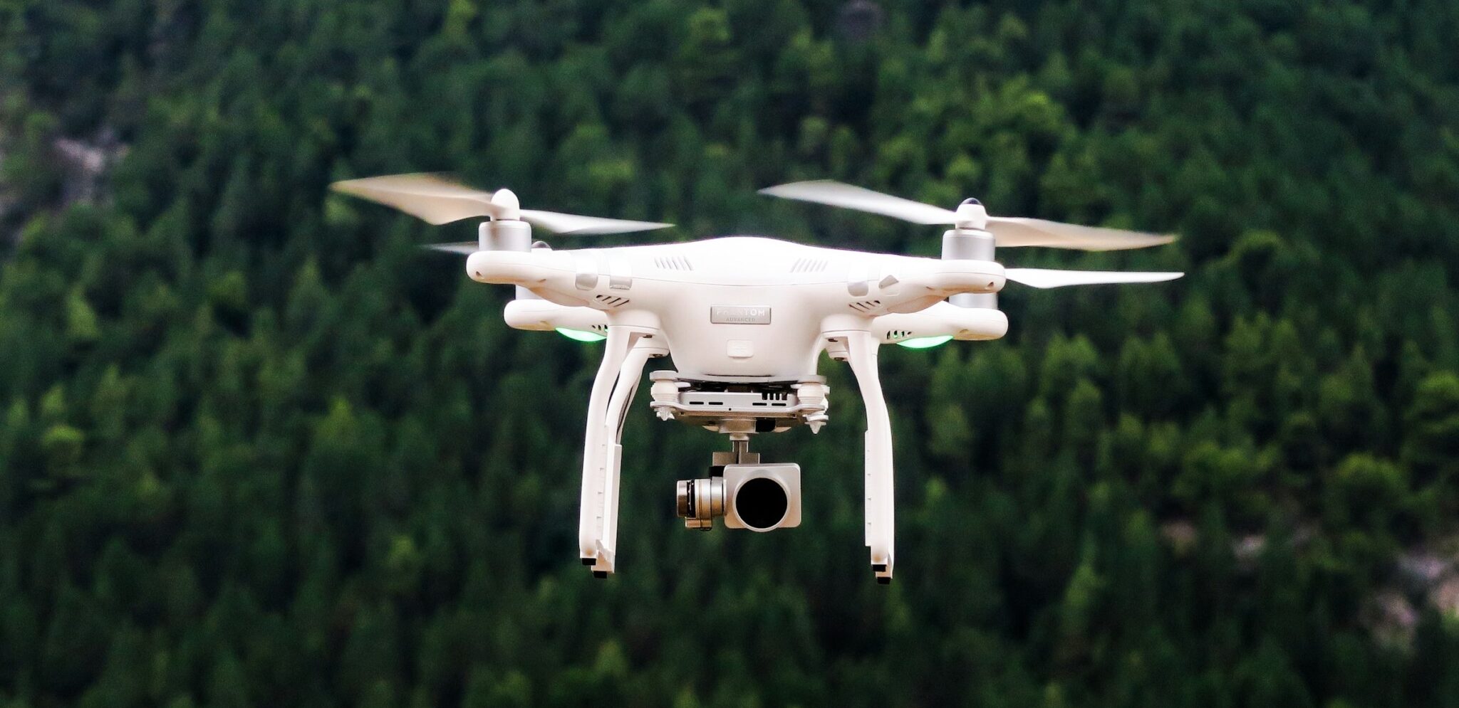 A close-up image of a white drone hovering in the foreground, with a dark forest in the background. GIS is increasingly integrating with technology such as AI, giving GIS Analysts the opportunity to work with cutting-edge technology.