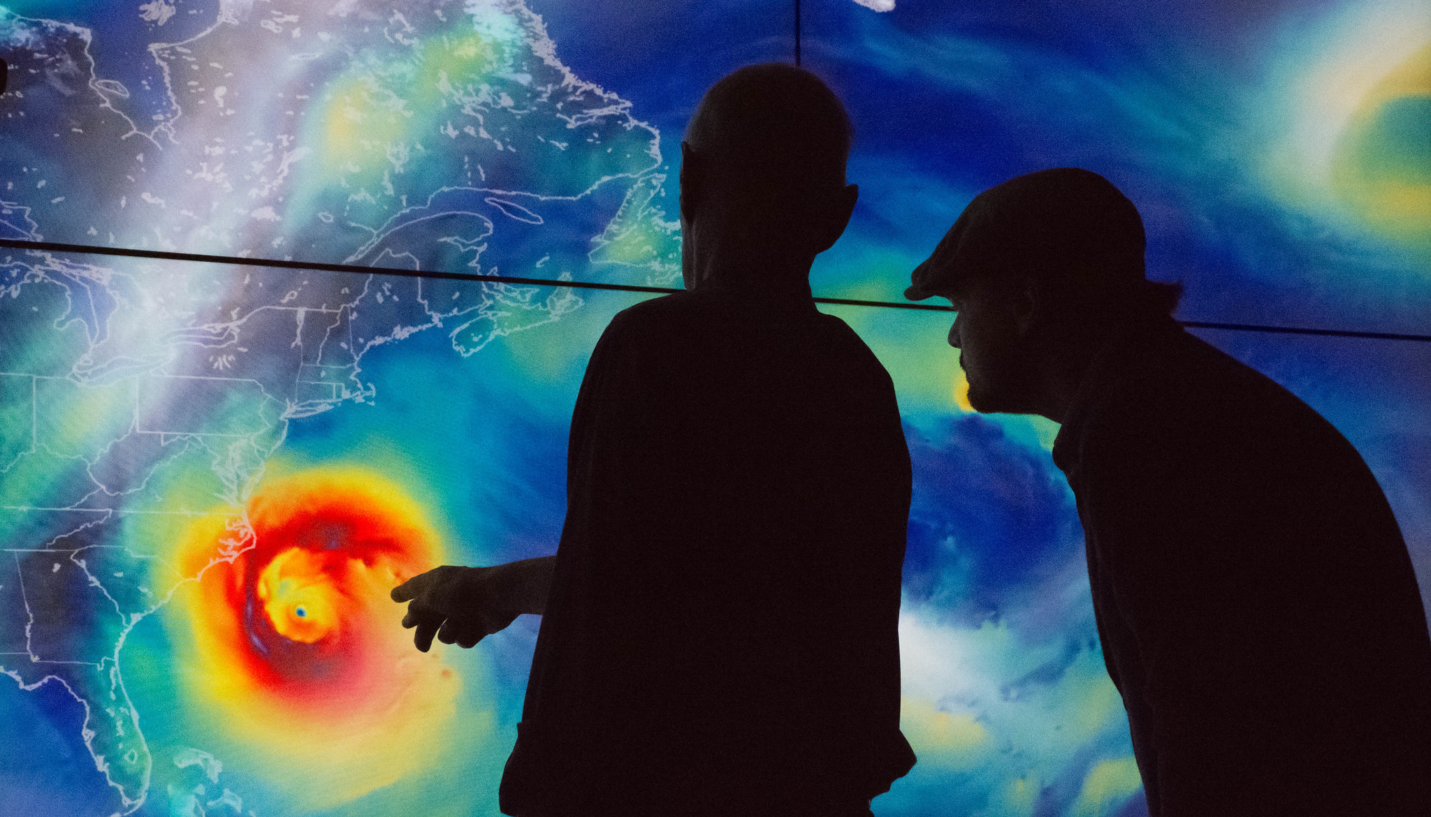 Two silhouetted men standing in front of a coloured image display related to climate change. It may be more likely to be able to work abroad in conservation in technical or specialist roles - such as climate science.