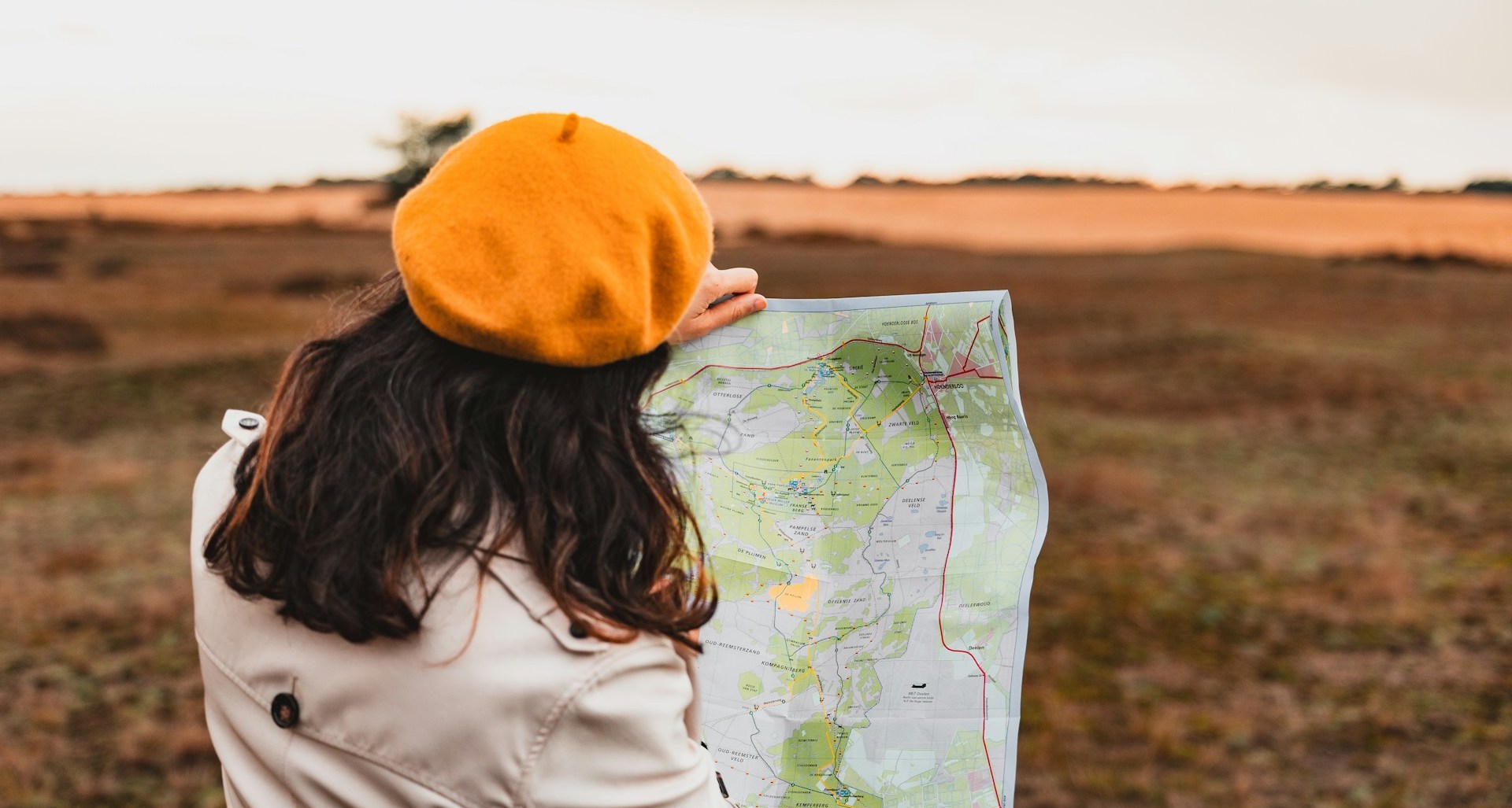 A woman with an organge cap and cream-coloured jacket standing outside holding a map. We've created this guide to help people navigate how to work abroad in conservation.