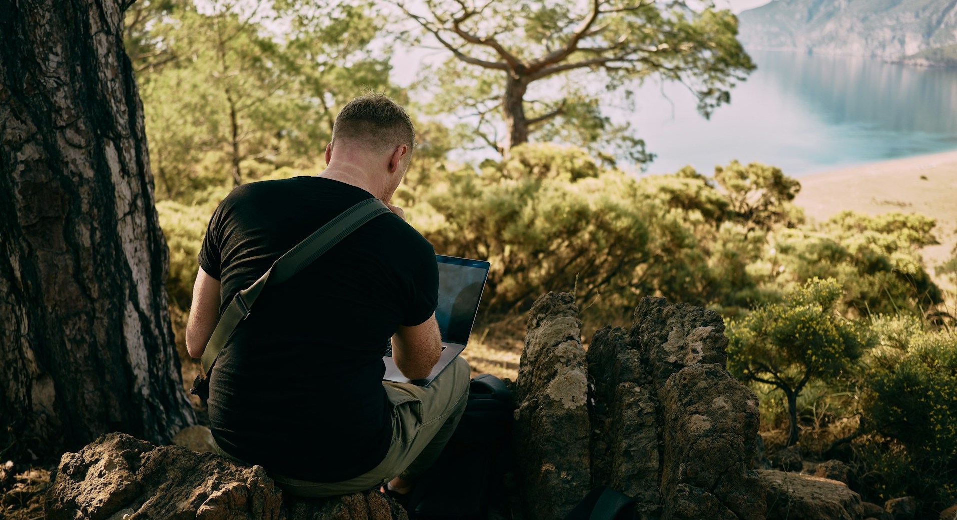 A man sitting outside with a bag strung across his back and a laptop on his knee. There are many ways to work abroad in conservation!