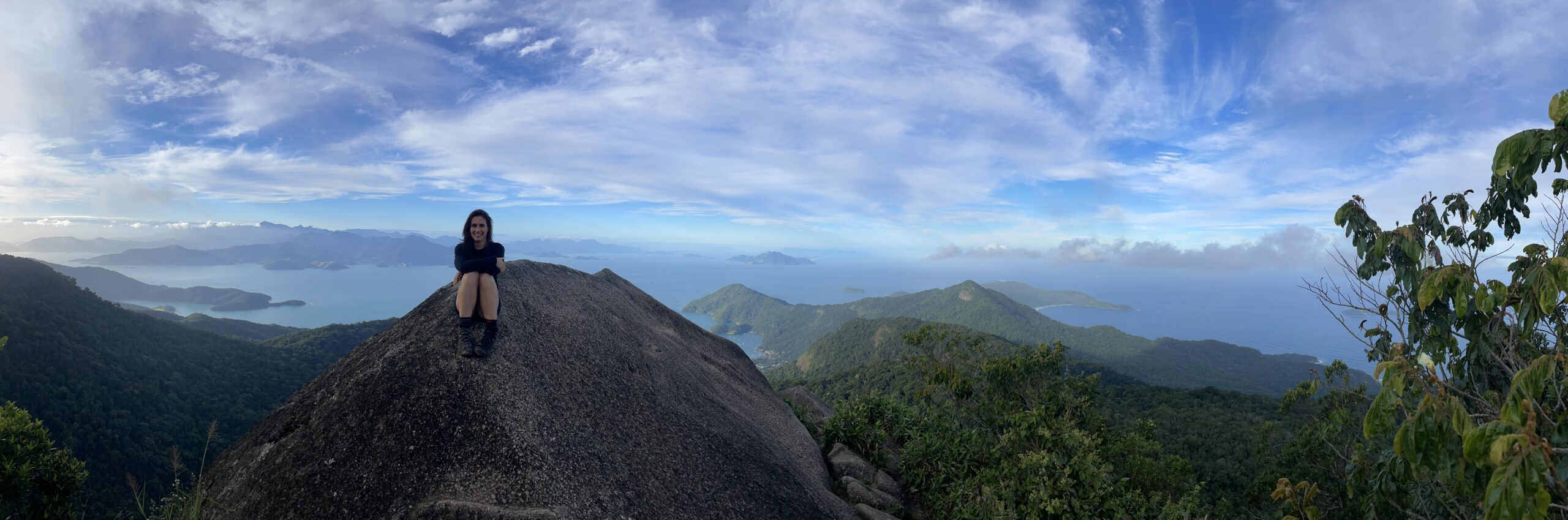 A woman sitting on a rock with a forest and ocean landscape behind her. One way to work abroad in conservation is having a remote job.