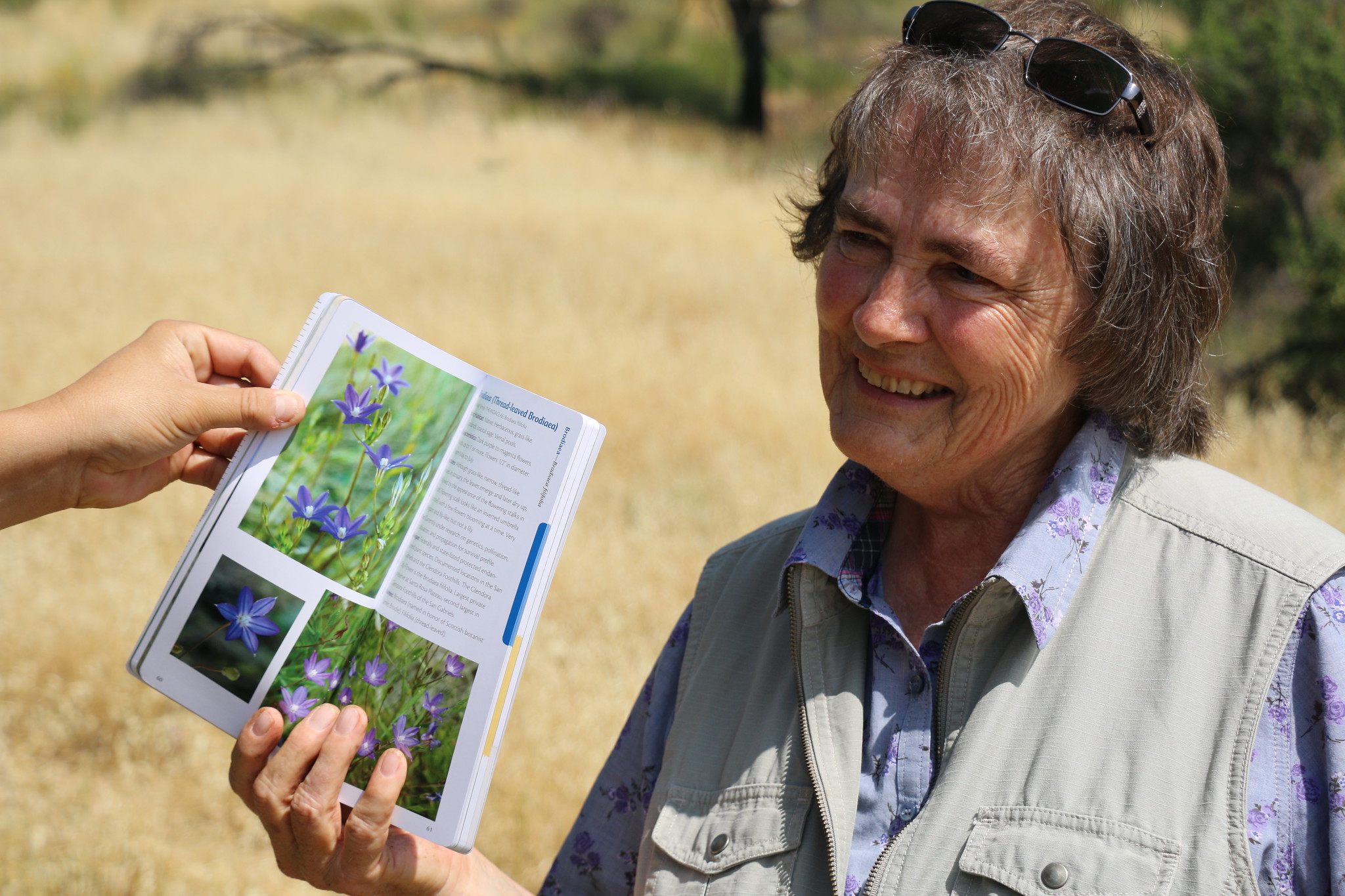 A smiling woman in a grassy landscape holding a plant identification book. Community-based conservation careers are open to conservationists of all ages and career stages.