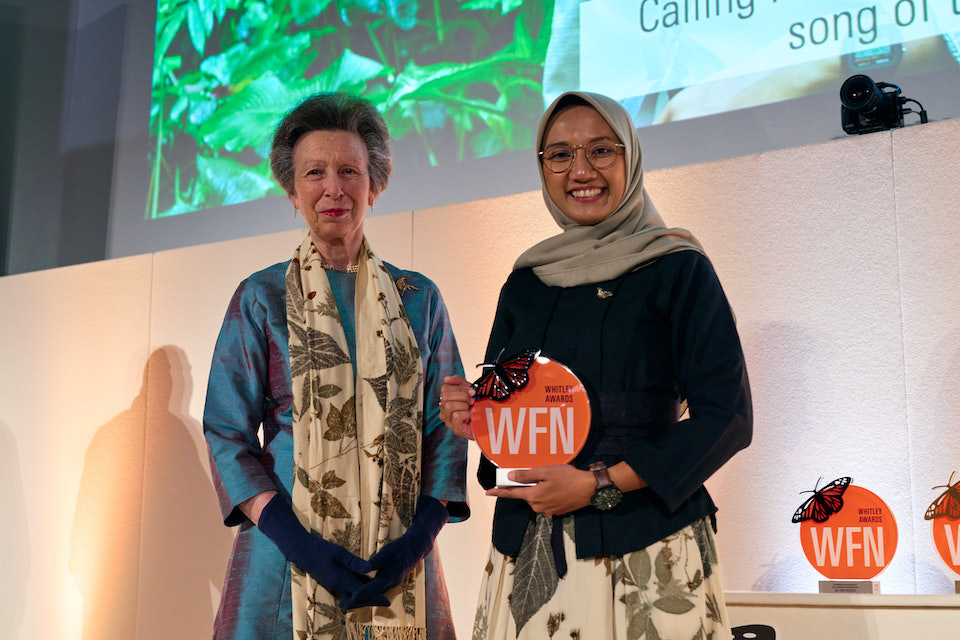 Two women standing next to one another in front of a stage, both smiling at the camera. One is Princess Anne, the other is Rahayu Oktaviani, who is holding an award she won.