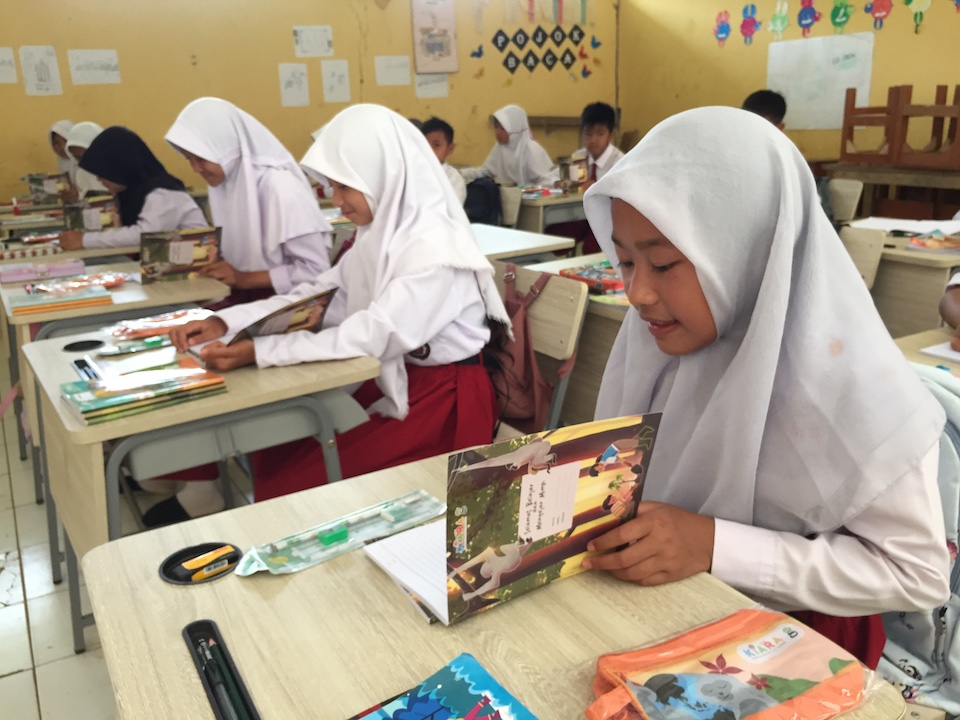 A group of children, sitting at desks in a classroom, reading a storybook on Javan gibbons.