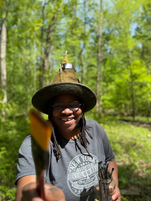 Jade in her element, paintbrush in hand, forest at her back. Creation begins outdoors, where stillness, observation, and wild spaces shape the stories that later unfold in ink.